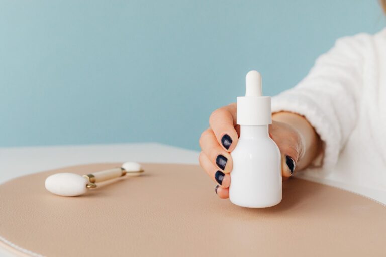 Bàn tay cầm chai serum dưỡng ẩm cạnh dụng cụ massage da